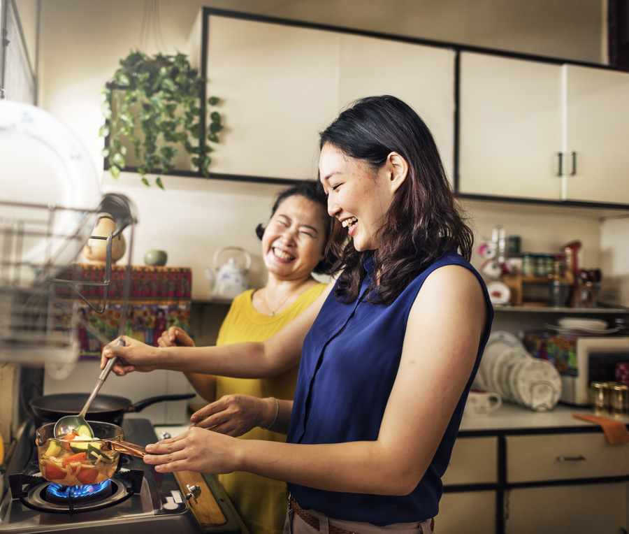 Filha sorridente fazendo receitas para o dia das mães junto com a irmã em frente ao fogão.